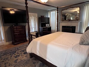 A bedroom with a four-poster bed, a television, a dresser, a fireplace, and a large mirror.