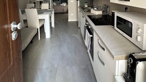 A modern kitchen with white cabinetry, a built-in microwave, and a coffee machine. There is a dining area with a white table and chairs, and a bed in the background. - La Casa dell' Arco nr 47: Authentic Local Stay in historic center with Jacuzzi (Triggiano)