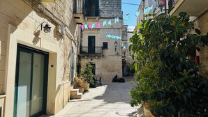 A narrow street with stone buildings, potted plants, and colorful flags. - La Casa dell' Arco nr 47: Authentic Local Stay in historic center with Jacuzzi (Triggiano)