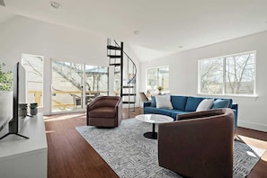 Una sala moderna con un sofá de cuero marrón, un sofá azul, una mesa de centro y una escalera en espiral.