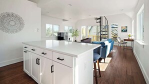 A spacious kitchen with a central island, a dining area with a blue sofa, and a spiral staircase leading to an upper level.