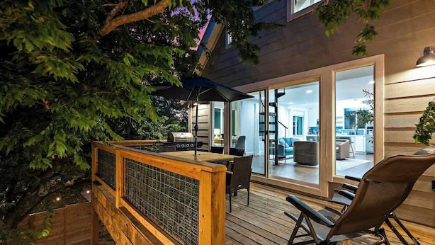 A wooden deck with a seating area, a glass door leading to an interior space, and a tree.