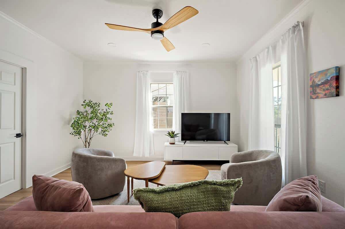 Un salon moderne doté d’un ventilateur de plafond, d’un téléviseur à écran plat, d’un canapé, de deux fauteuils, d’une petite table et d’une plante en pot.