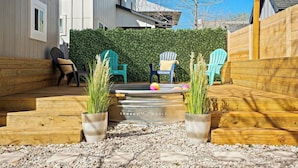 A backyard with a wooden deck, two Adirondack chairs, a small pool, and potted plants.