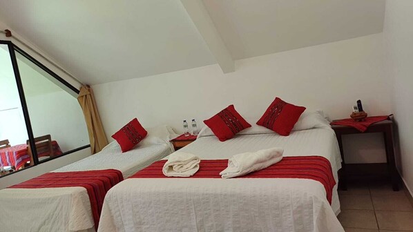 Ein Hotelzimmer mit zwei Betten, rot-weiß gestreifter Bettwäsche, einem kleinen Tisch mit Telefon und Wasserflaschen sowie einem Fenster mit Blick.