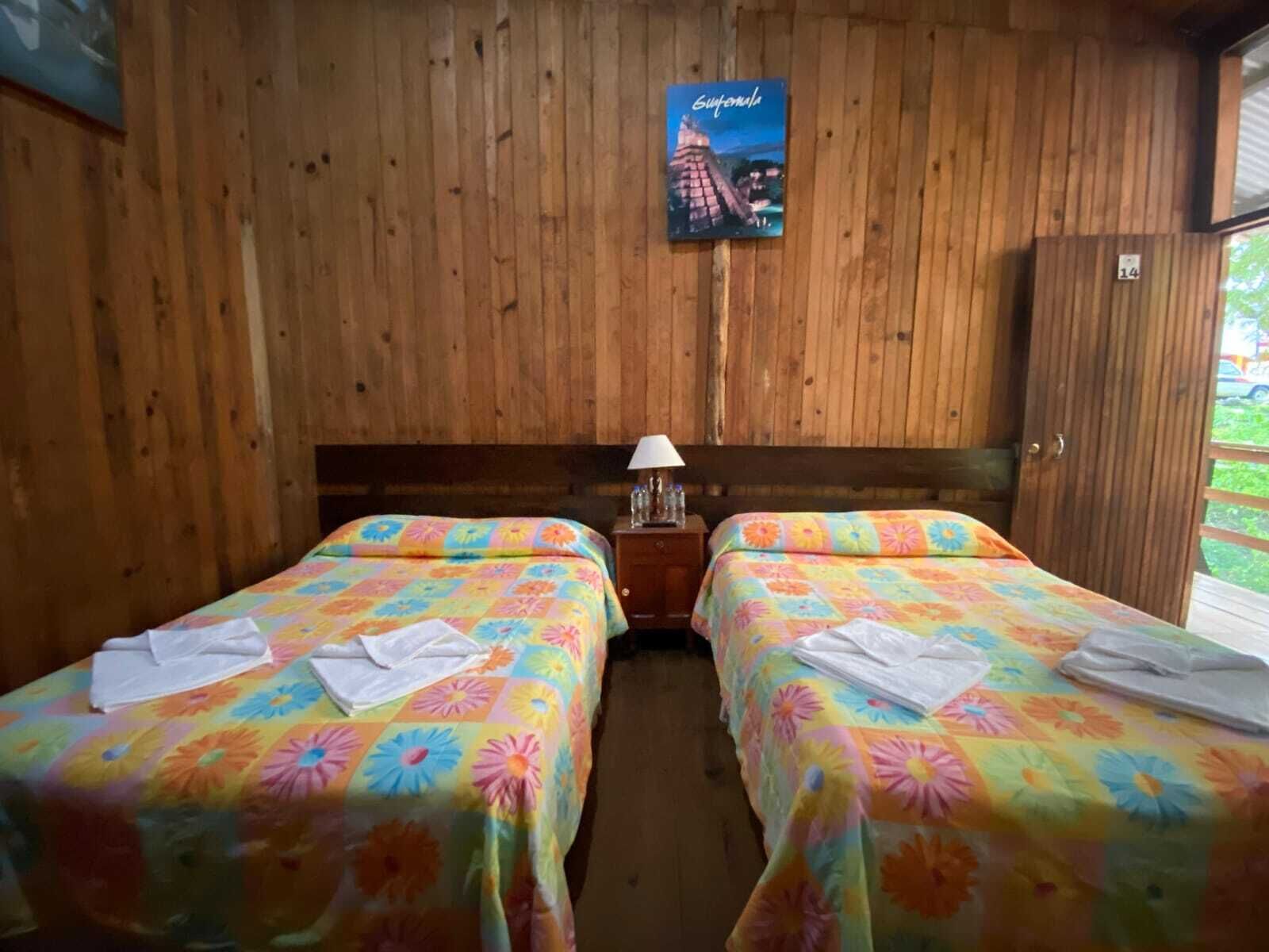 Une chambre avec deux lits, des murs en bois, une table de chevet avec une lampe et un tableau encadré au mur.