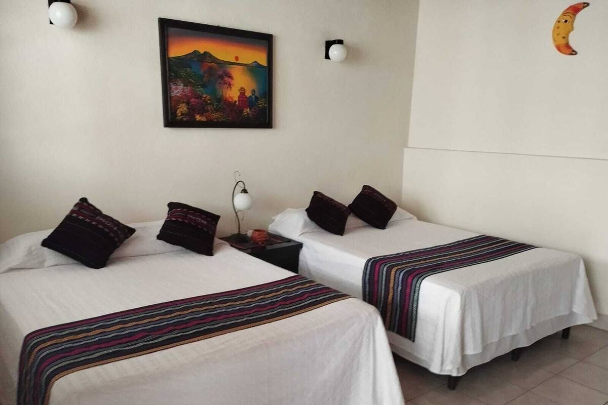 Une chambre d’hôtel avec deux lits, une table de chevet, une lampe, un tableau et une horloge murale.
