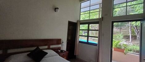 Un dormitorio con cama de madera, una mesita de noche, una ventana y una puerta abierta que da a un espacio exterior.