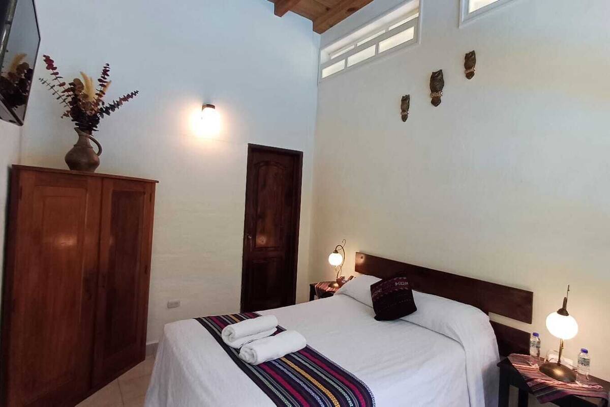 Une chambre à coucher comprenant un lit, une table de chevet, des lampes fixées au mur, une armoire en bois et une porte.
