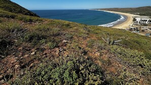 A coastal landscape with a beach, a building with multiple windows, and a clear sky. - Ocean View-Brand New Modern Contemporary Home- Walk to Beach-Safe and Secure (todos santos , bcs)