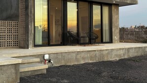 A modern building with large sliding glass doors, a concrete exterior, and a small outdoor seating area with two chairs and a table. - Ocean View-Brand New Modern Contemporary Home- Walk to Beach-Safe and Secure (todos santos , bcs)