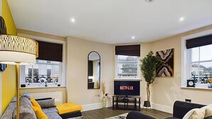 Una sala de estar moderna con un sofá, una mesa de centro, un televisor y un ventanal con vistas a un edificio.