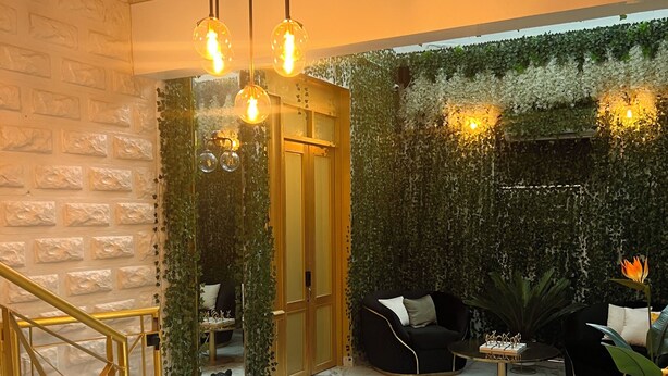 Un intérieur moderne avec un sol en marbre, un canapé en cuir noir, un portail à cadre doré et un mur vert orné de plantes grimpantes.