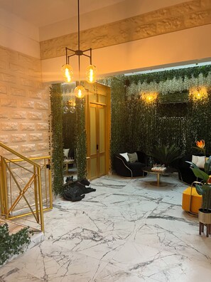 Un intérieur moderne avec un sol en marbre, un canapé en cuir noir, un portail à cadre doré et un mur vert orné de plantes grimpantes.