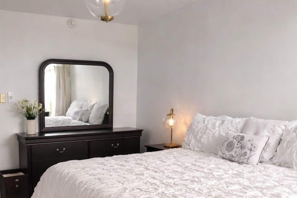 Une chambre à coucher avec un grand lit, une commode, un miroir et une lampe de chevet.