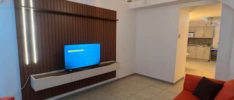 A modern living room with a flat-screen TV on a wooden panel wall, a red sofa, and a ceiling light fixture.