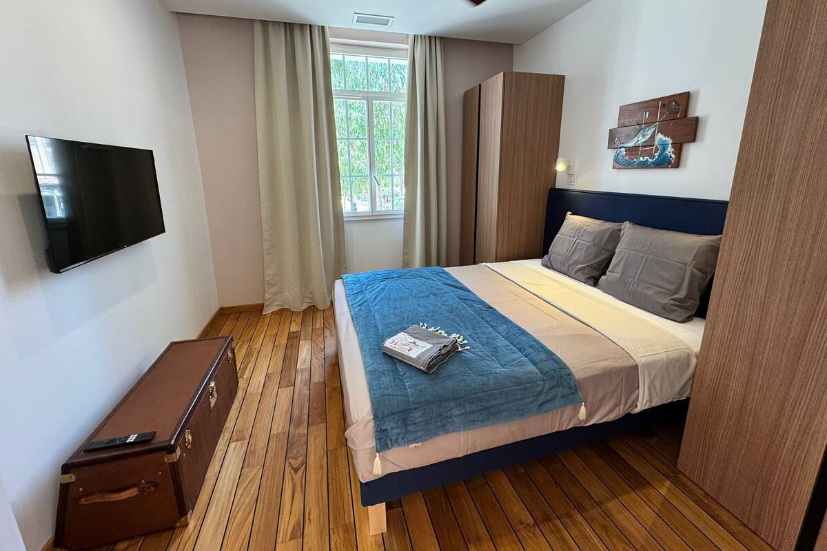 Un dormitorio con cama, televisor, maleta y ventana con cortinas.
