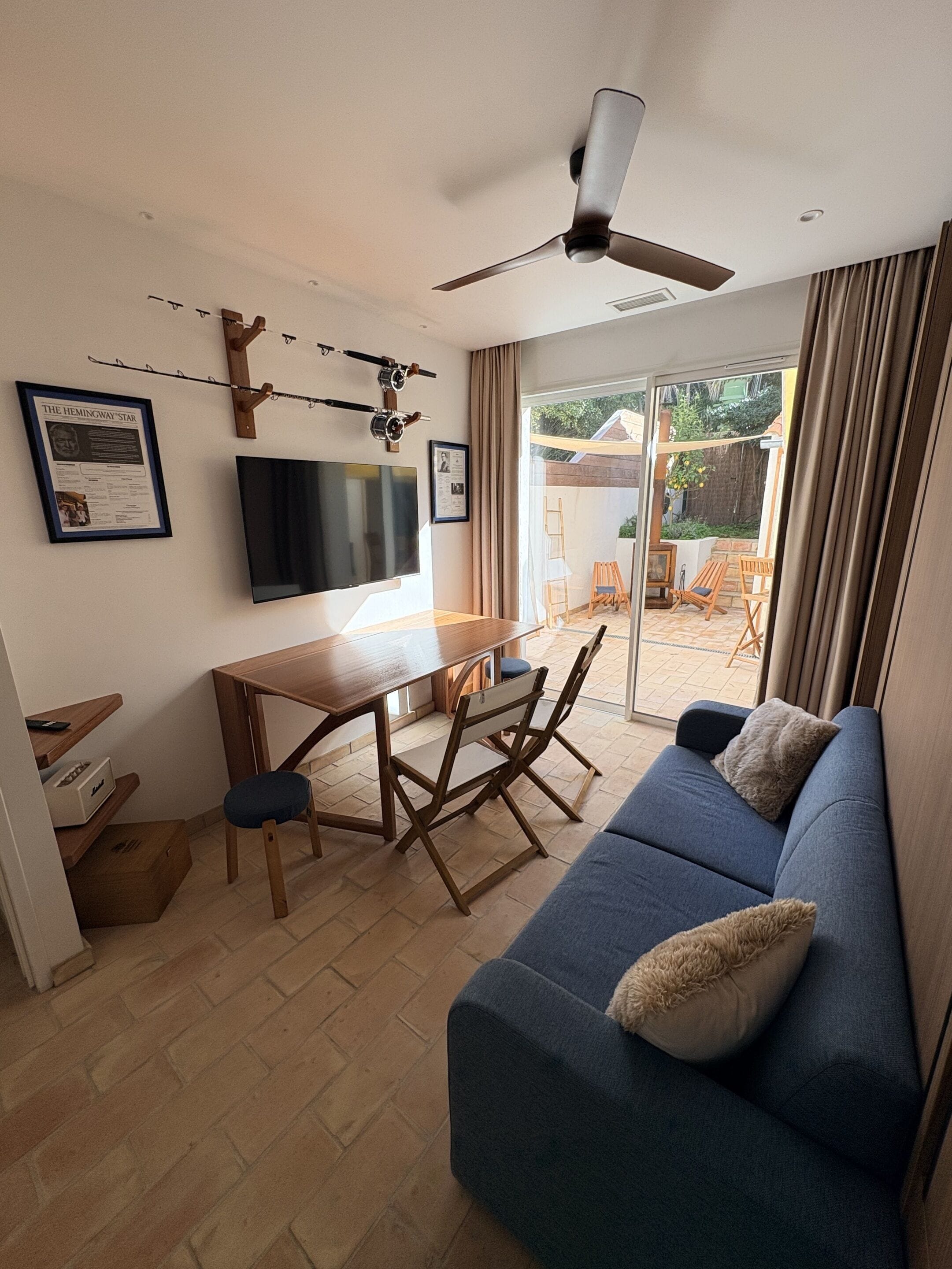 A modern living room with a blue sofa, wooden dining table, and ceiling fan.