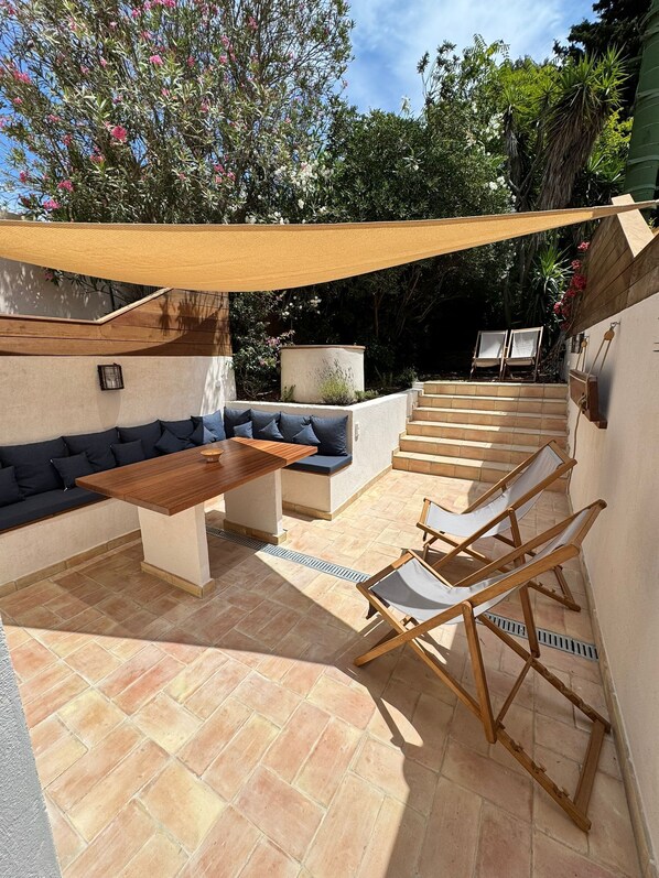 An outdoor patio with a wooden table, a sofa, and two chairs. There is a staircase leading to a higher level.