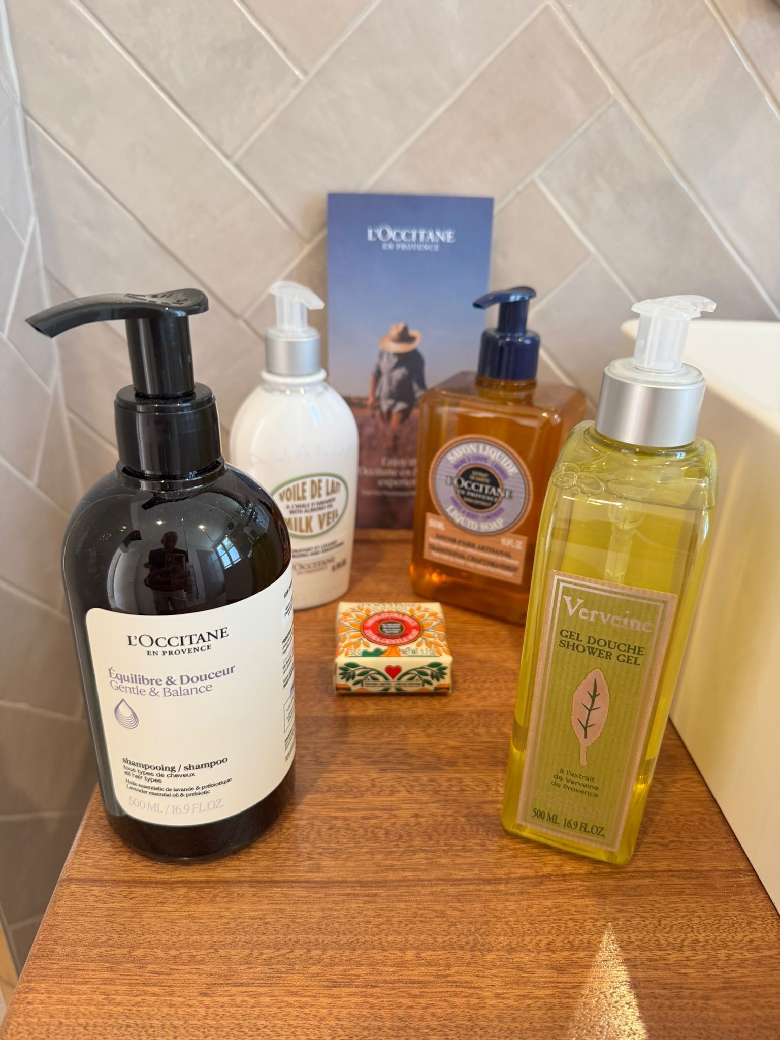 A bathroom shelf with various toiletries including a black bottle of shampoo, a white bottle of soap, a yellow bottle of shower gel, and a box of soap bars.