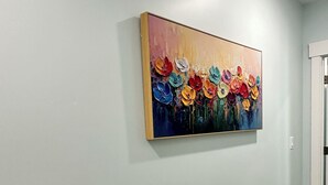Een gang met een lichtblauwe wand en een vloerbedekking. Een kleurrijk schilderij van bloemen hangt aan de muur.