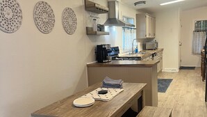 Moderni keittiö, jossa on puinen pöytä ja penkki, sisäänrakennettu uuni ja mikroaaltouuni.