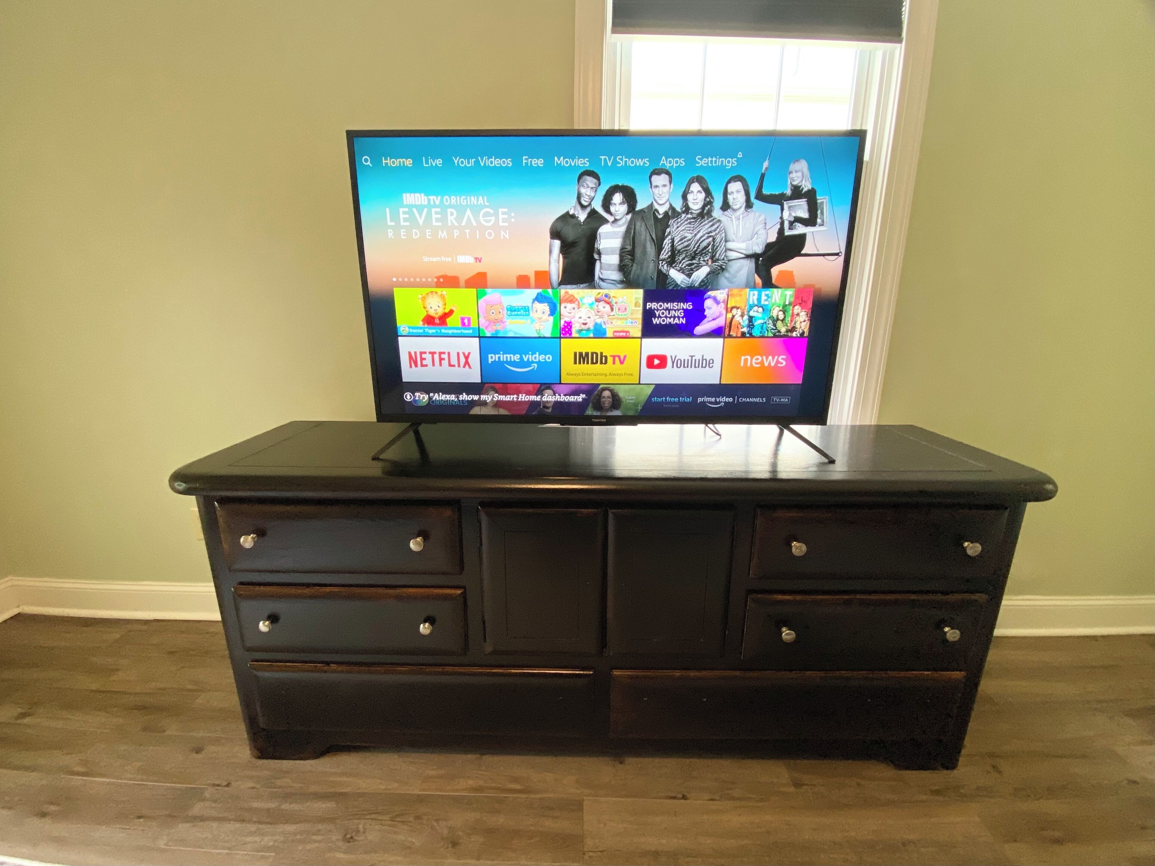 Un téléviseur posé sur un meuble en bois, dont l’écran affiche différents services de diffusion en continu.