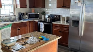 Una cocina con armarios de madera, un refrigerador de acero inoxidable, una encimera de granito y un ventilador de techo.