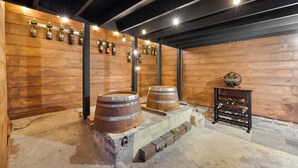 Una bodega rústica con paredes de madera, dos barricas grandes y una estantería para vinos.