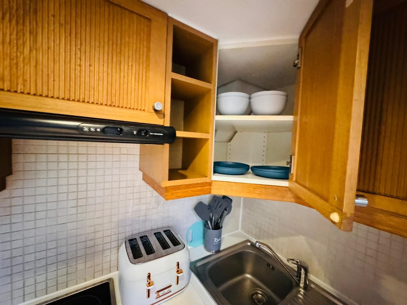 A compact kitchen with a toaster, a sink, and wooden cabinets.
