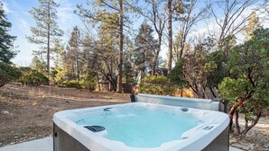 Un bain à remous dans un jardin, entouré d’arbres et doté d’une terrasse en bois.