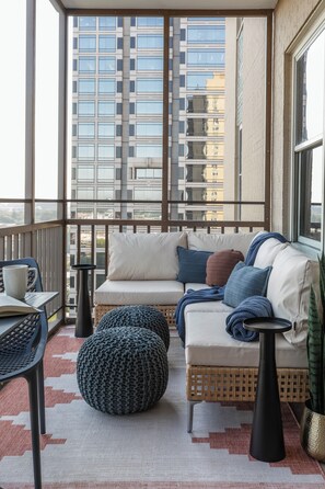 Ein Balkon mit einer Couch, einem Hocker und einem Tisch mit Blick auf eine Stadtlandschaft.