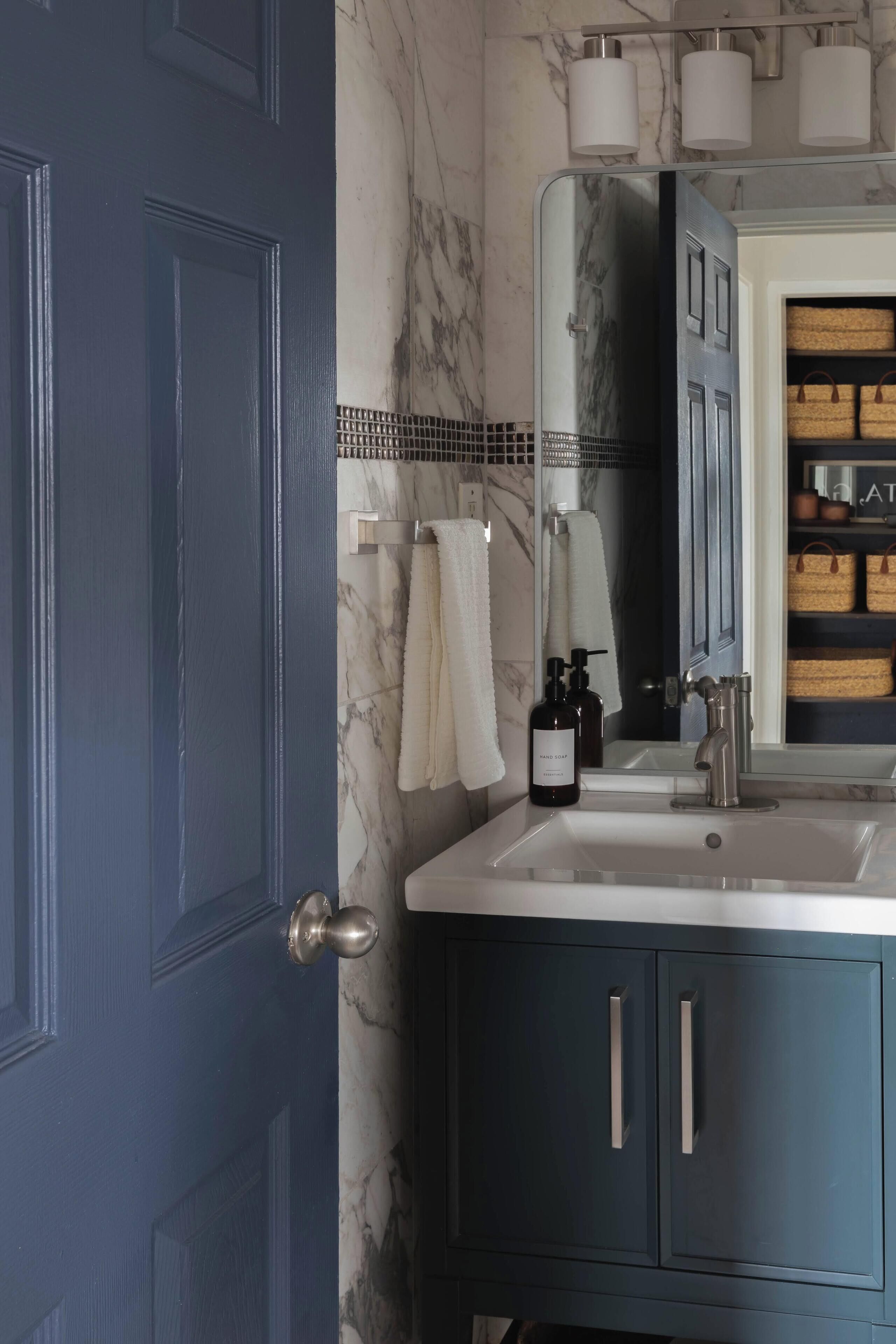 Un baño con una puerta azul oscuro, un lavamanos blanco y un espejo encima.