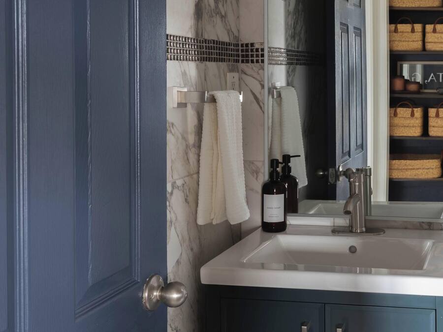 A bathroom with a dark blue door, a white sink, and a mirror above it.