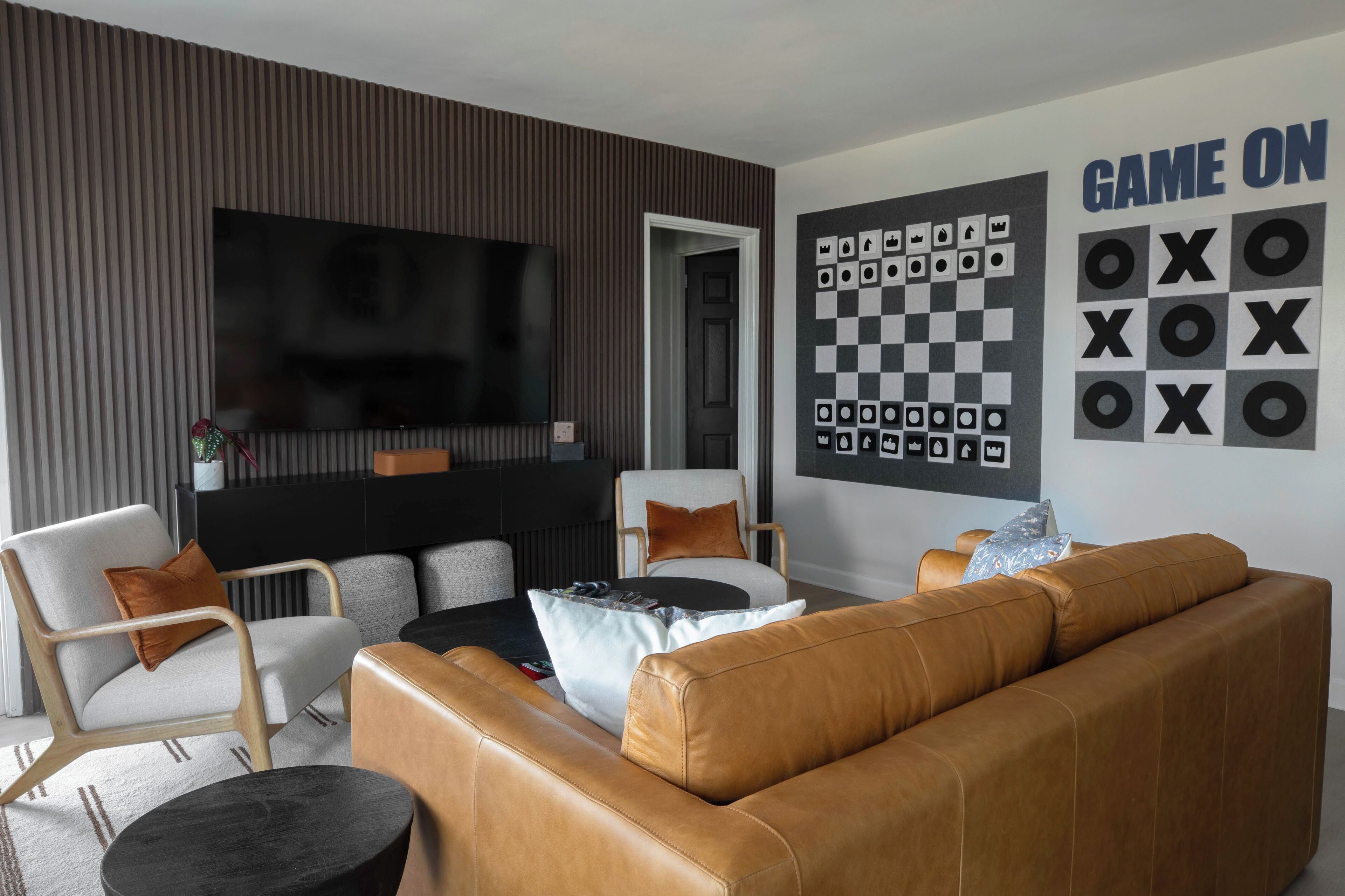 Una sala moderna con un televisor de pantalla plana grande, una pared con un juego de mesa de cuadros y un sofá de cuero marrón.