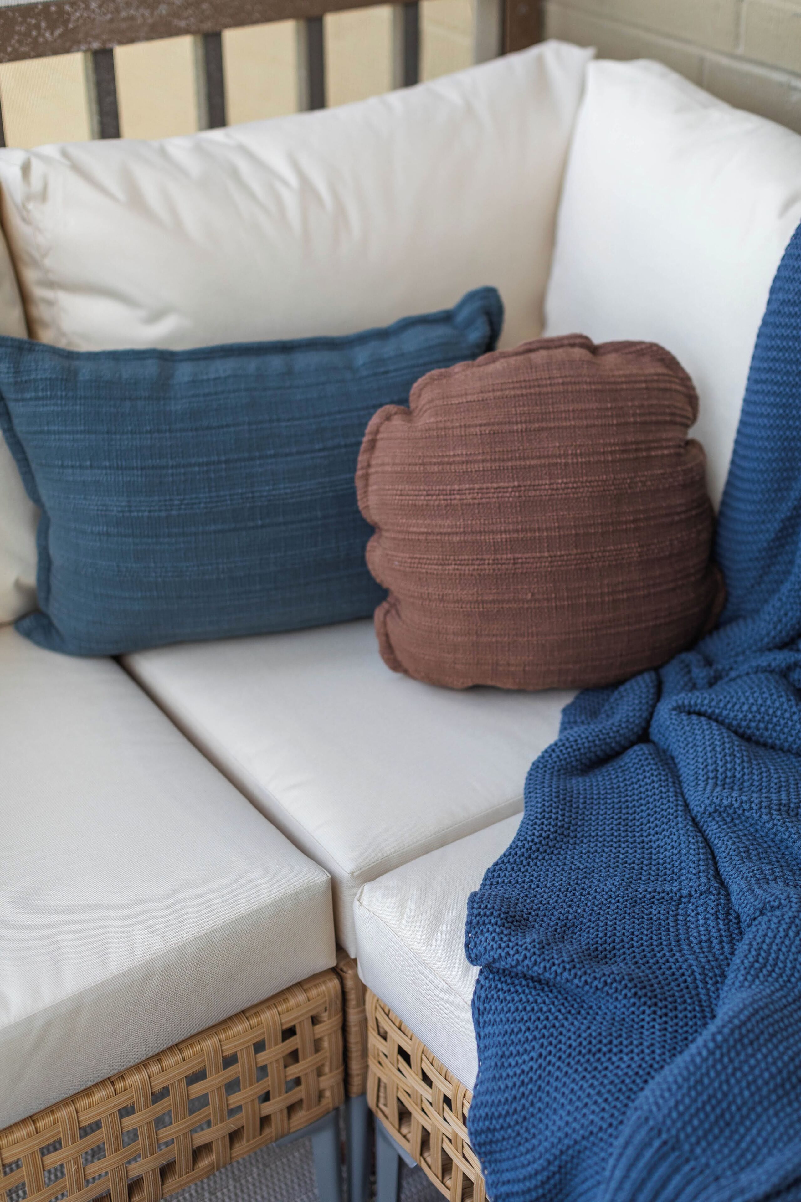 A wicker sofa with white cushions and a blue knitted blanket.