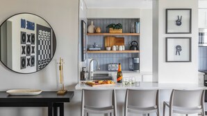 A modern kitchen with a central island, bar stools, and a round mirror. - Downtown ATL Condo Balcony (Atlanta)
