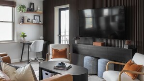 A modern living room with a large flat-screen TV mounted on a dark wall, a comfortable sofa, a coffee table, and a small side table with a plant. - Downtown ATL Condo Balcony (Atlanta)