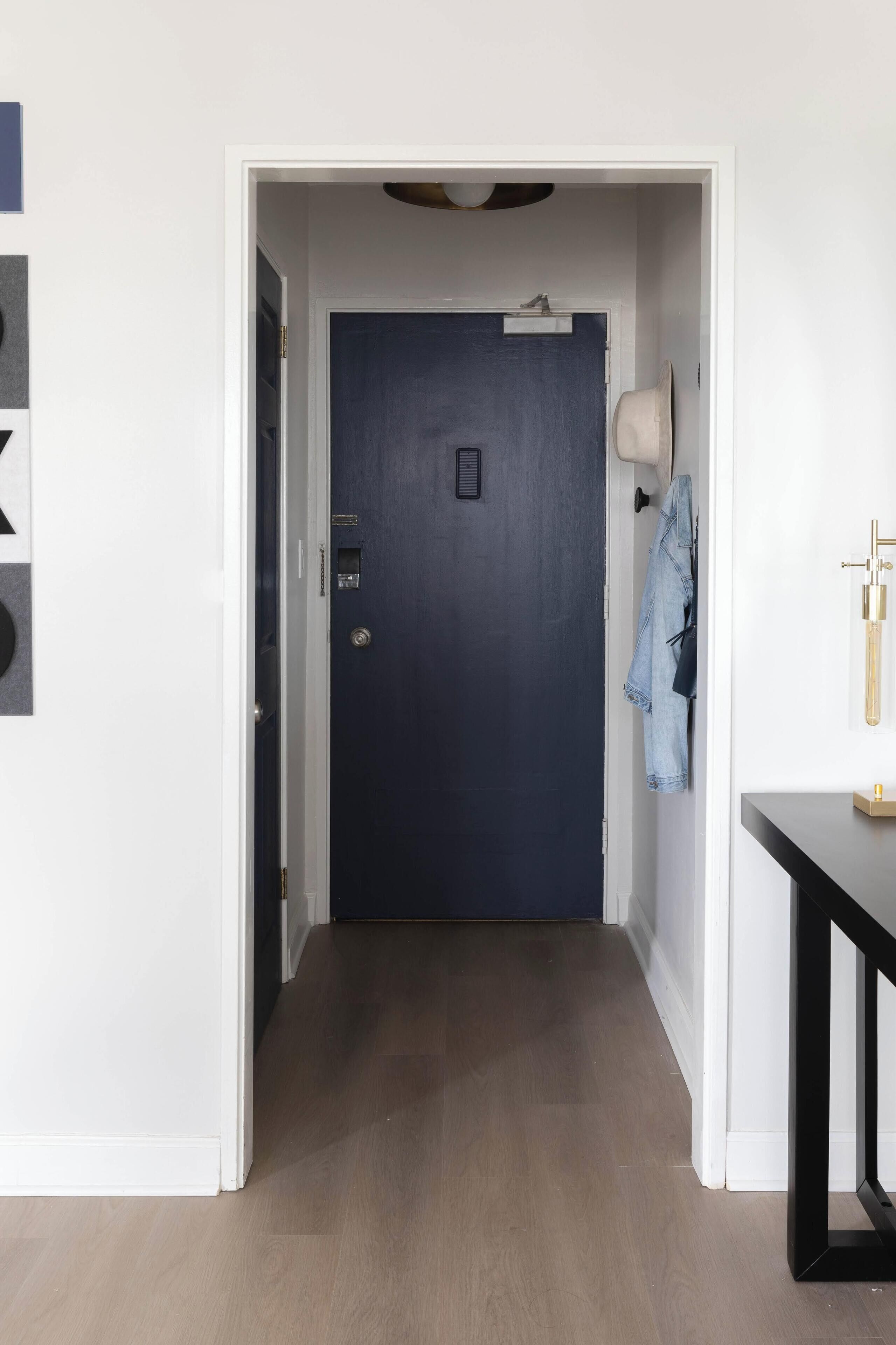 A hallway with a dark blue door, a light switch, and a coat hanging on the wall.