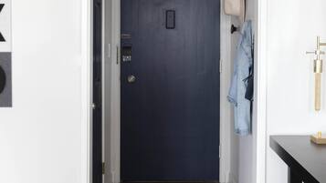 A hallway with a dark blue door, a light switch, and a coat hanging on the wall.