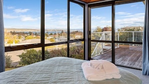 A bedroom with a large window offering a view of a residential area and a body of water.
