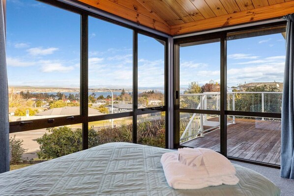 A bedroom with a large window offering a view of a residential area and a body of water.