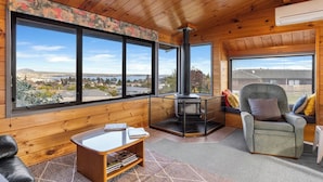 A cozy cabin interior with a large window offering a scenic view, a fireplace, a comfortable seating area, and a small table.