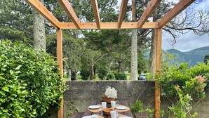 A wooden pergola with a table set for a meal, surrounded by greenery and trees. - LAKEVIEW GREEN PARADISE By Azores HomeMade (Ponta Delgada)