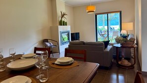 A dining area with a wooden table set for a meal, a sofa, and a TV in the background. - LAKEVIEW GREEN PARADISE By Azores HomeMade (Ponta Delgada)