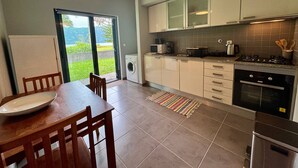A modern kitchen with a dining area, a washing machine, and a view of greenery outside. - LAKEVIEW GREEN PARADISE By Azores HomeMade (Ponta Delgada)