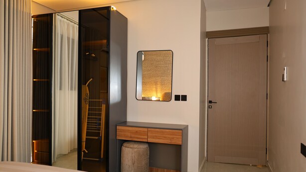 A hotel room with a bed, a vanity with a mirror, a wooden desk, a small stool, and a door. - Lovely apartment with AC in vibrant Riyadh (Riyadh)