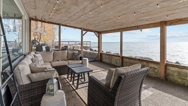 A covered outdoor seating area with wicker furniture, a wooden ceiling, and a view of the water. - Lakeview Escape. Hot Tub, Sauna, Screened Porch. Birding Paradise. Wineries! (Amherstburg)