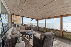 A covered outdoor seating area with wicker furniture, a wooden ceiling, and a view of the water. - Romantic Winter Escape with Lake Views: Hot Tub, Infrared Sauna (Amherstburg)