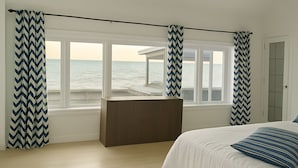 A bedroom with a bed, a wooden bench, and a view of the sea through large windows. - Lakeview Escape. Hot Tub, Sauna, Screened Porch. Birding Paradise. Wineries! (Amherstburg)